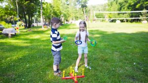 Two kids enjoying a ring toss game outdoors in a sunny park setting.